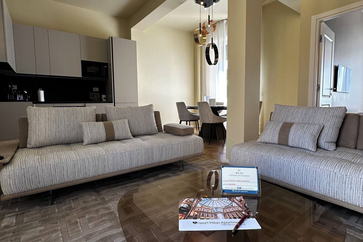 Un espacio habitable amplio con un moderno juego de sofás, una mesita de centro y una cocina al fondo.