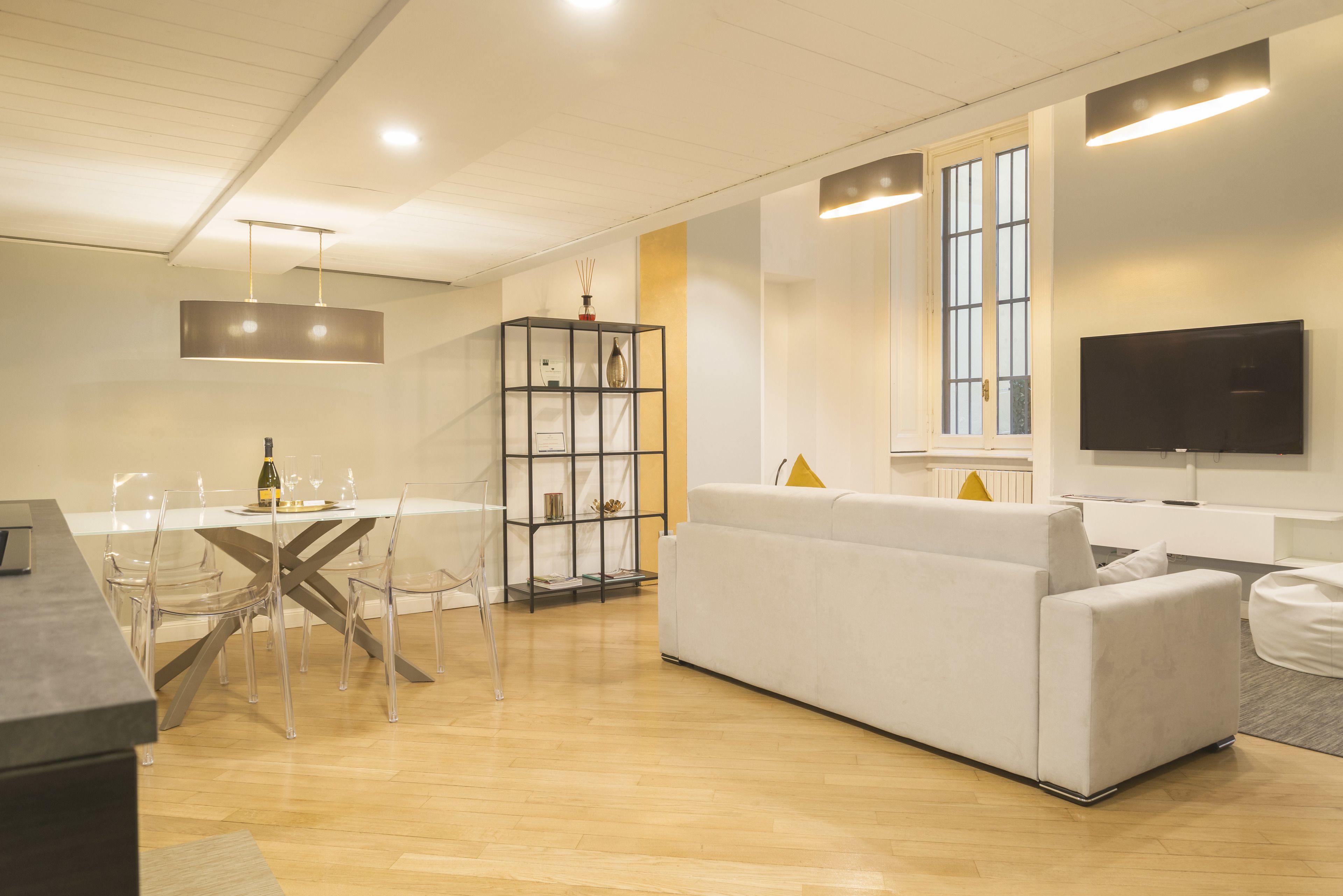 A modern living room with a white sofa, a dining table with chairs, and a TV mounted on the wall.