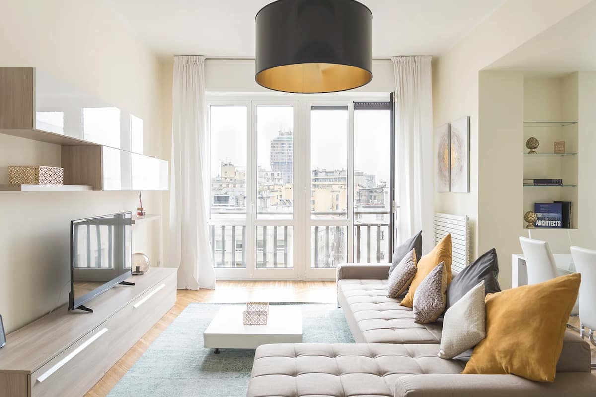 Una sala de estar moderna con sofá, mesa de centro, televisor y vista a la ciudad a través de grandes ventanales.