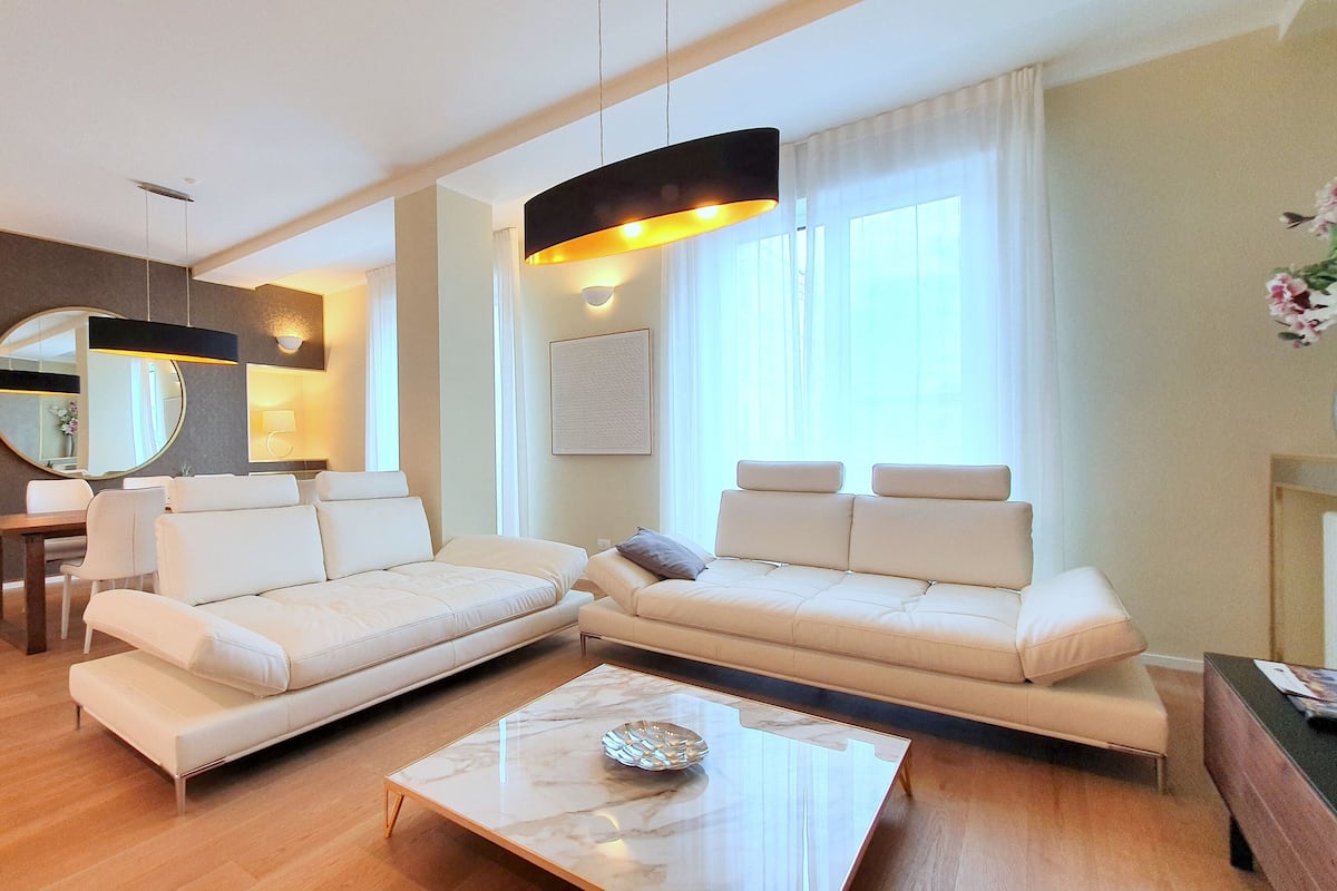 Una sala de estar moderna con un sofá seccional, una mesa de centro de vidrio y un ventanal con cortinas.