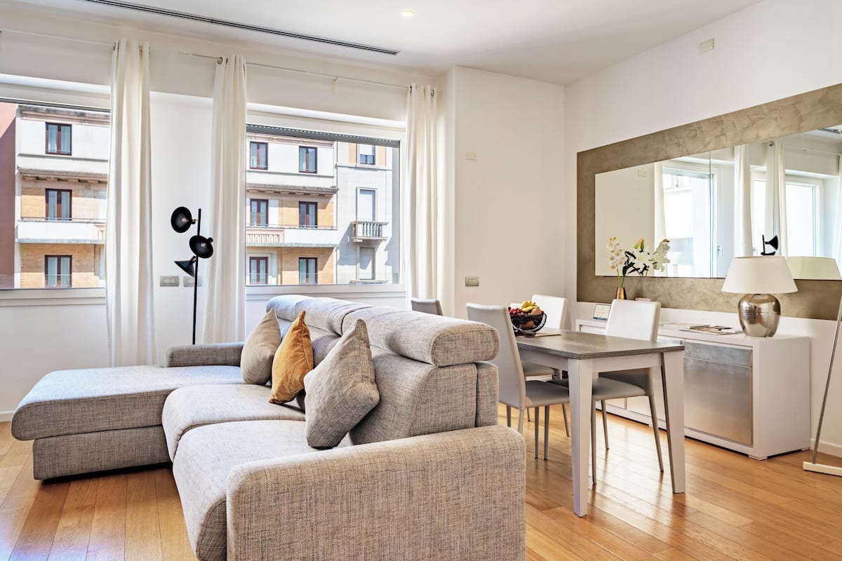 Una sala moderna con un sofá seccional gris, una mesa de comedor y un espejo grande.