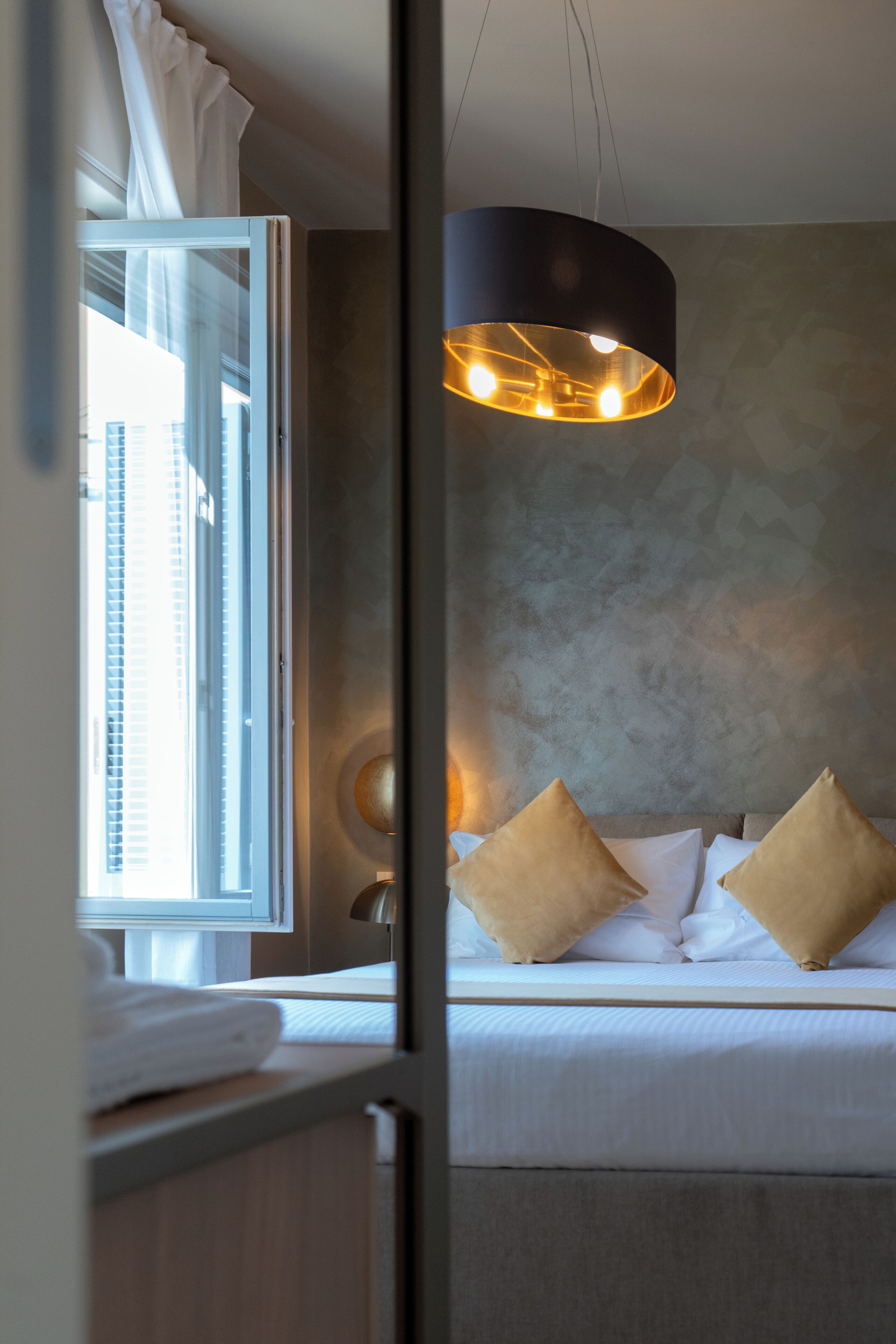 Une chambre à coucher avec un lit, des oreillers, un luminaire suspendu et une fenêtre avec des rideaux.