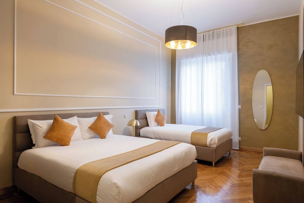 Habitación de hotel con dos camas, un sofá, un espejo y una lámpara colgante.