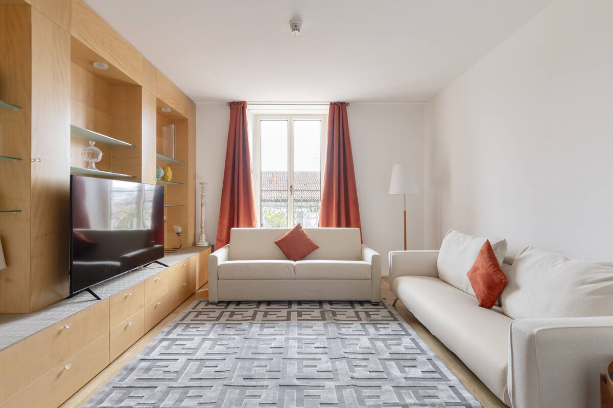 Una sala de estar moderna con un sofá, televisor, armarios de madera y un tapete estampado.