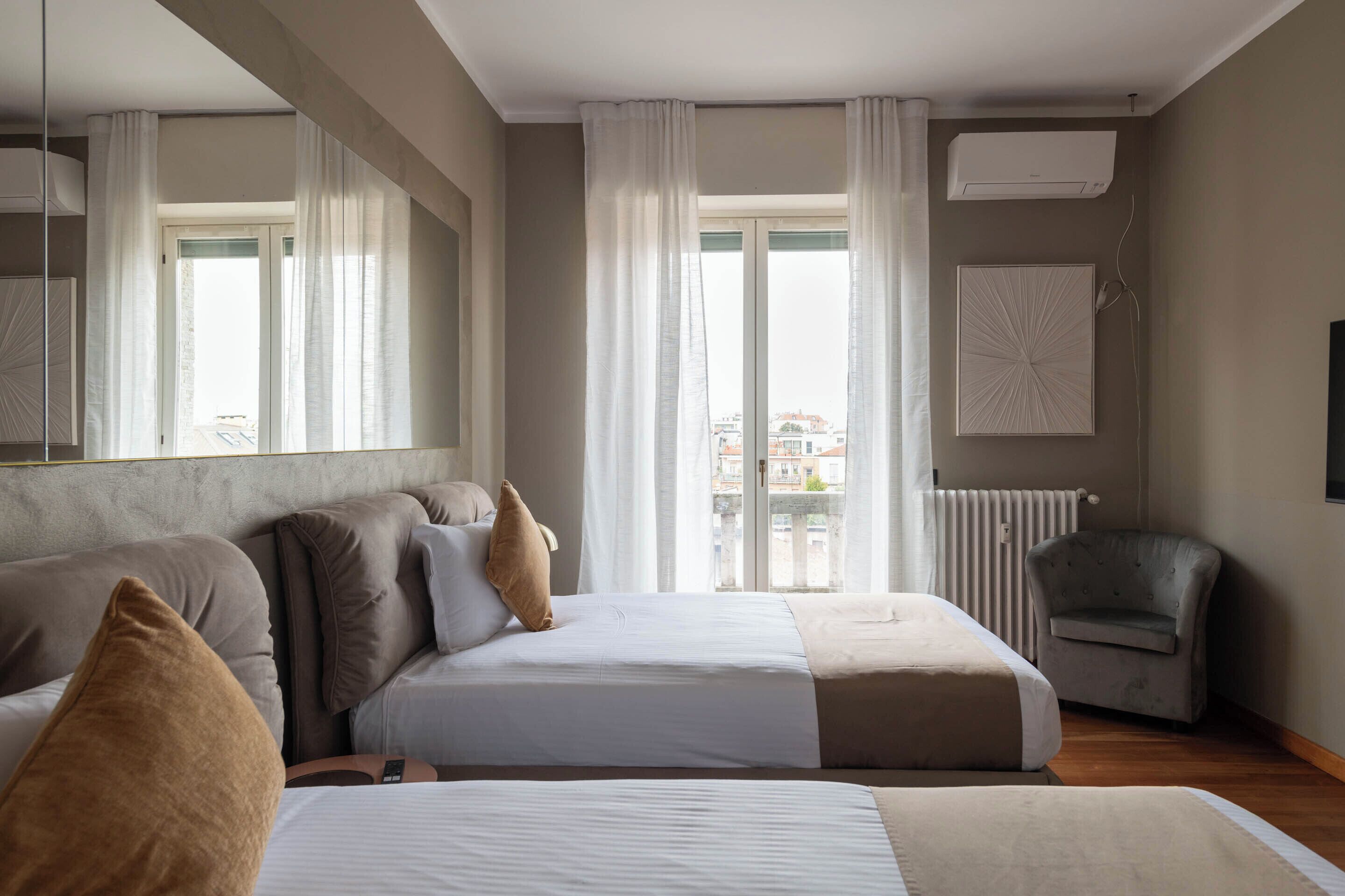 A hotel room with two beds, a chair, a large mirror, and a view of the city through the window.