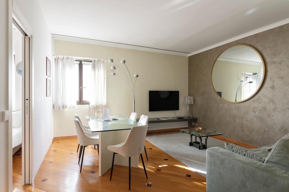Una sala de estar moderna con una mesa de comedor de vidrio, un sofá, un televisor y un espejo grande.