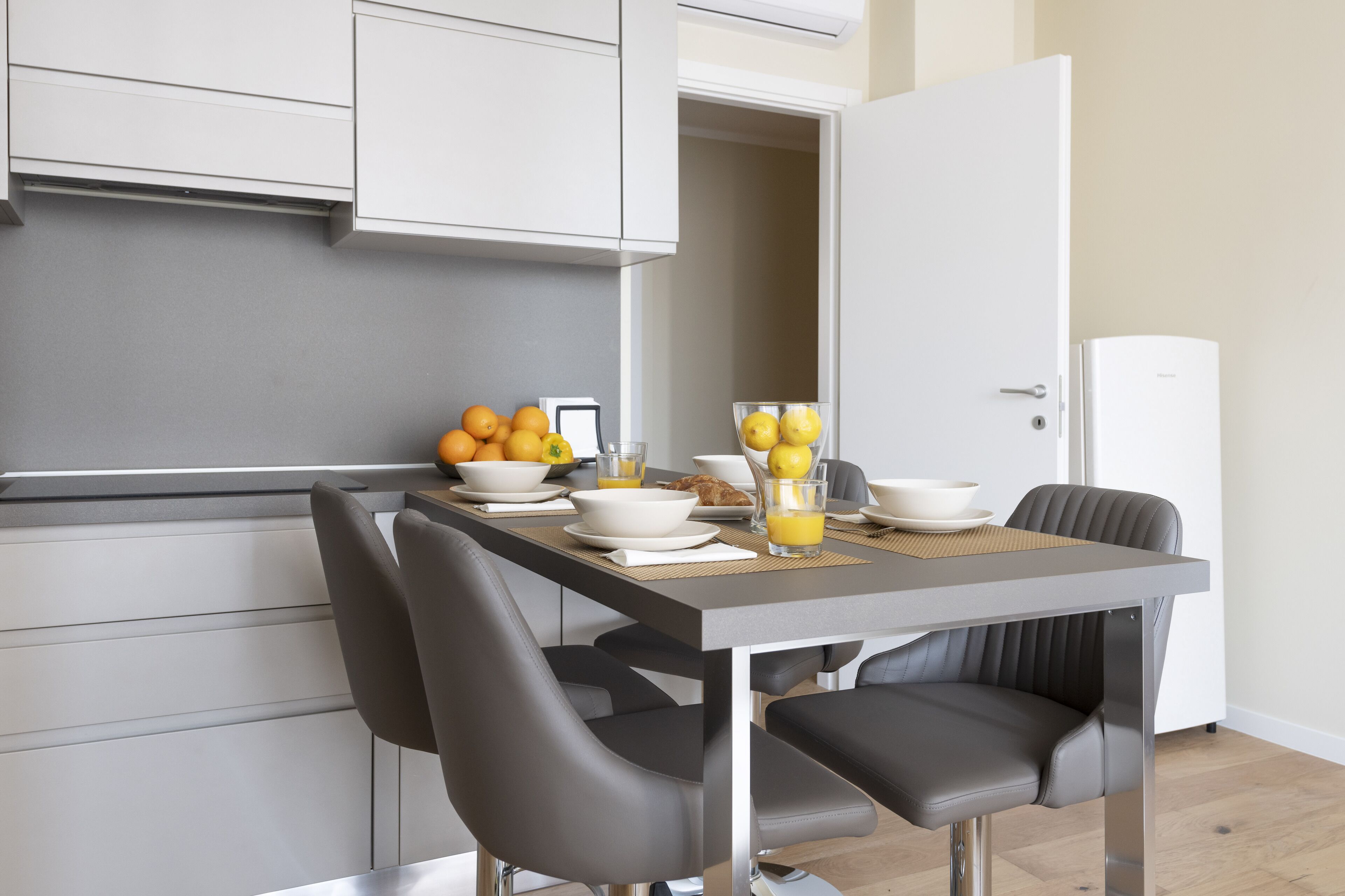 Una cocina moderna con una mesa de desayuno dispuesta, que incluye frutas, un tazón de cereal y un vaso de jugo de naranja.