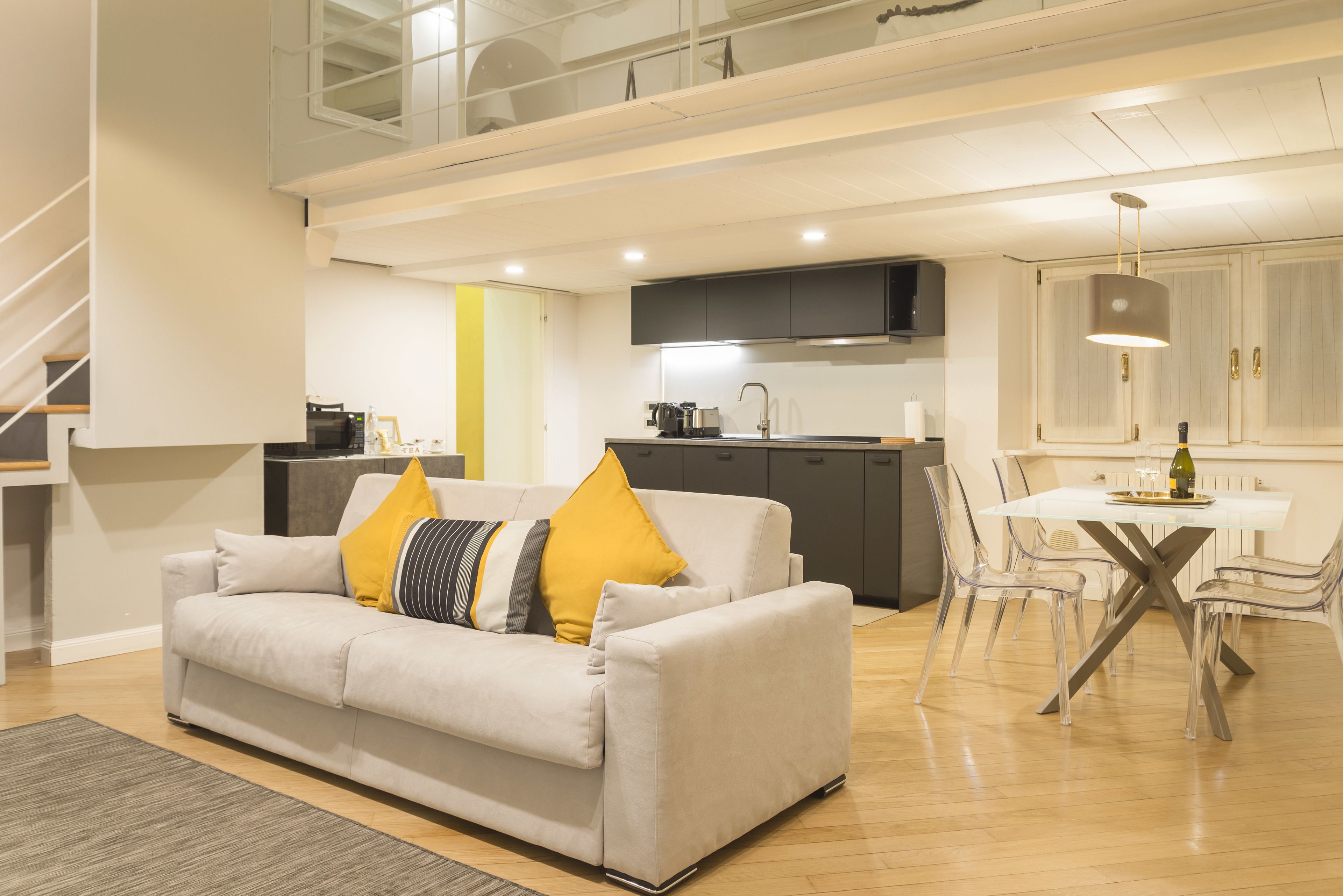 A modern living room with a sofa, a dining table with chairs, a kitchen area, and a staircase.
