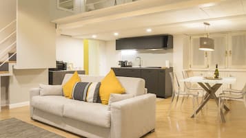 A modern living room with a sofa, a dining table with chairs, a kitchen area, and a staircase.