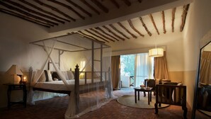 A bedroom with a four-poster bed, a sitting area with a table and chairs, and a large window with curtains.