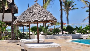 A pool area with lounge chairs, a thatched umbrella, and palm trees.