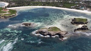 An aerial view of a coastal area with clear turquoise waters, rocky outcrops, and a sandy beach.