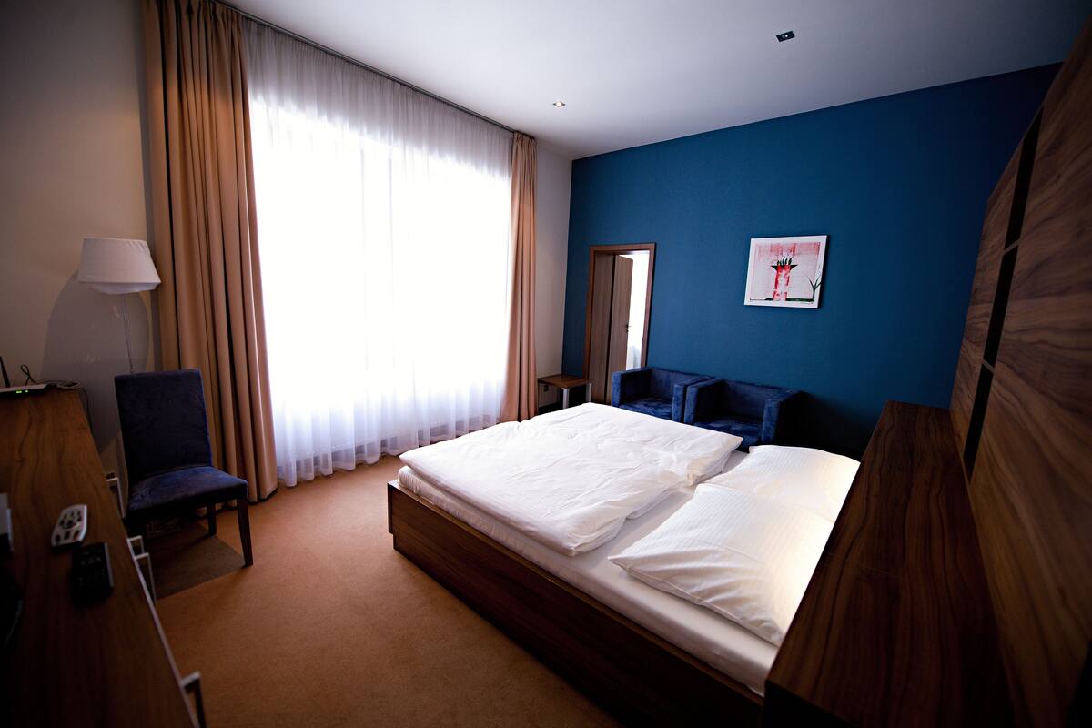 Ett hotellrum med en stor säng, ett skrivbord med en lampa, en stol och en tavla på väggen.
