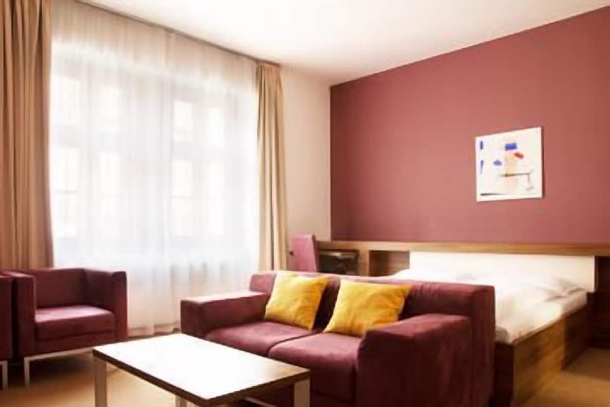 Ett hotellrum med en säng, en soffa, ett bord och ett fönster med gardiner.