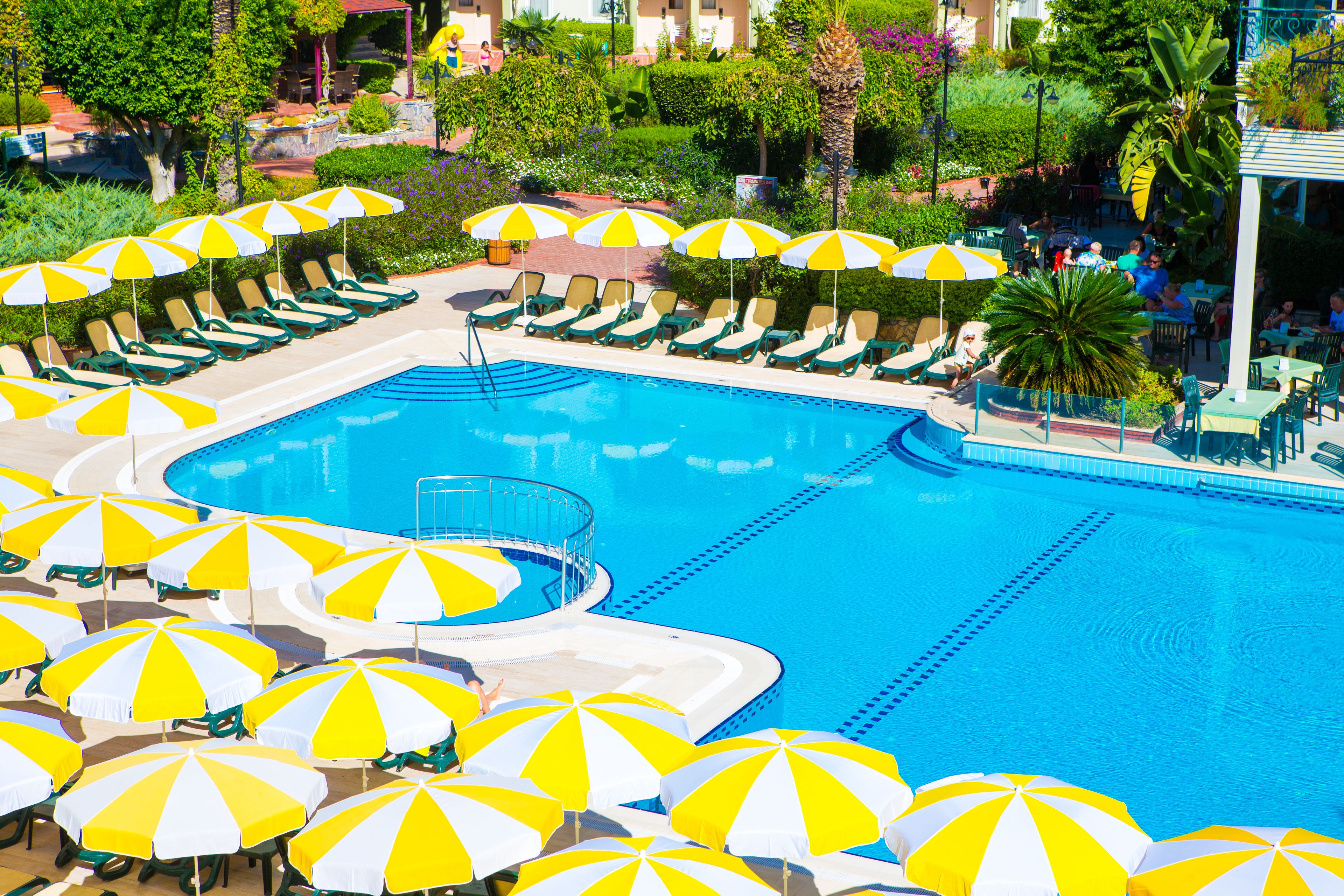 A pool area with multiple yellow and white umbrellas, lounge chairs, and a clear blue pool.