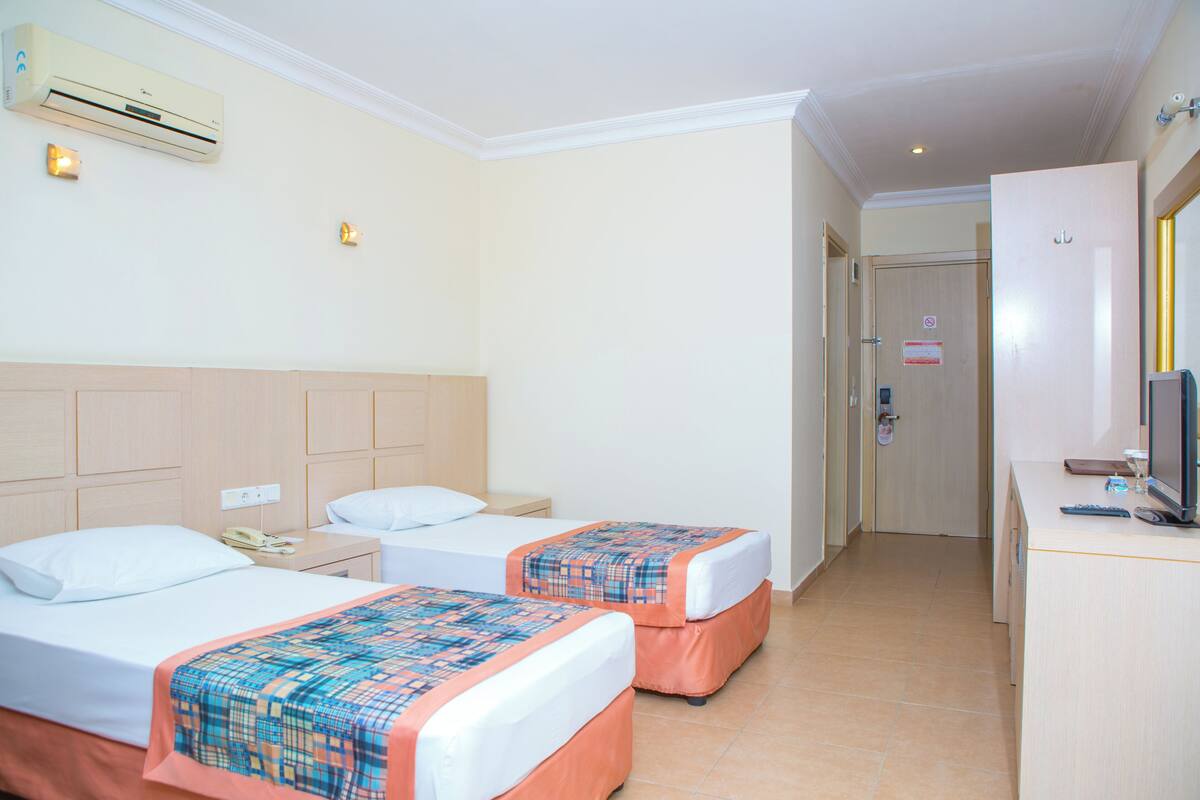 A hotel room with two beds, a desk, a TV, and an air conditioning unit.