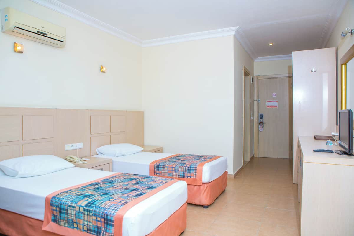 A hotel room with two beds, a desk with a computer, and an air conditioning unit.