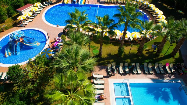 A large outdoor swimming pool with a water slide, surrounded by palm trees and sun loungers. - Gardenia Beach Hotel - All Inclusive (Alanya)