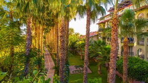 A courtyard with palm trees, a pathway, and a building with balconies. - Gardenia Beach Hotel - All Inclusive (Alanya)