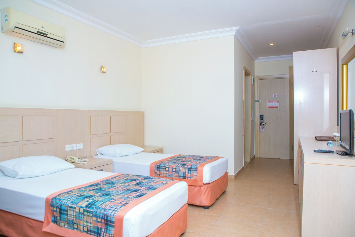 A hotel room with two beds, a desk with a computer, and an air conditioning unit.