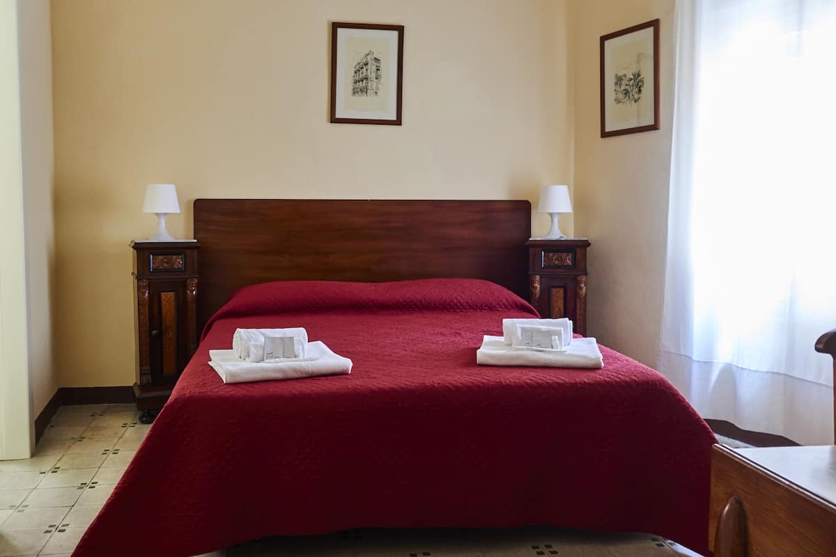 A neatly made bed with a red bedspread, two bedside tables with lamps, and two framed pictures on the wall.