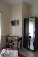 Una habitación con cama, escritorio, silla, televisor y armario.