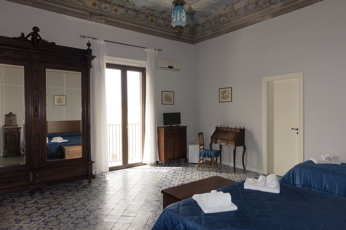A hotel room with a large mirror, a bed with blue bedding, a wooden desk, a chair, and a small table.