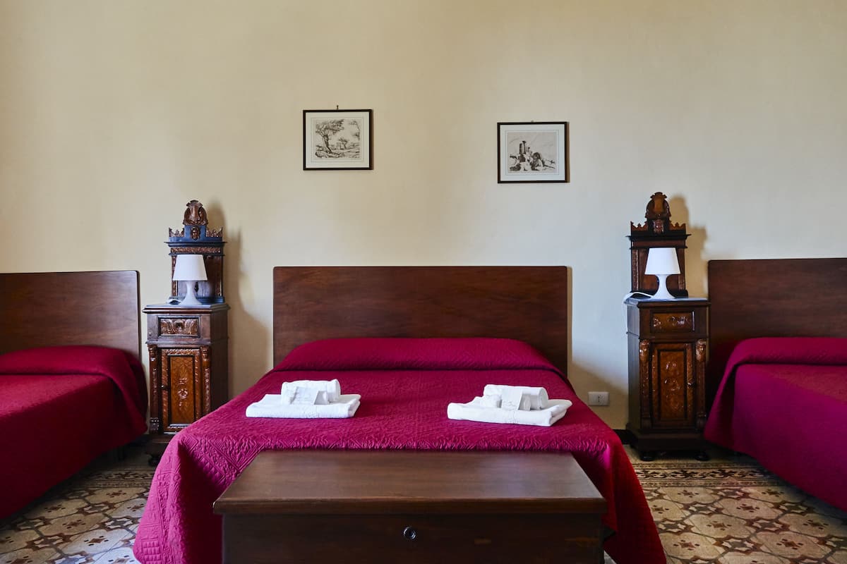 A hotel room with a wooden headboard, two beds with red bedding, a wooden nightstand with a lamp, and two framed pictures on the wall.
