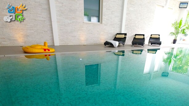 An indoor swimming pool with clear water, lounge chairs, and a potted plant. - My-Cocoon (Court-Saint-Etienne)