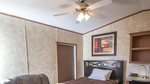 Ein Schlafzimmer mit einem Bett, einem Relaxsessel, einem Schreibtisch und einem Deckenventilator.