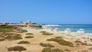 A beach resort with dome-shaped huts, a large building, and a clear blue sky. - Marsa Shagra Village (Marsa Alam)