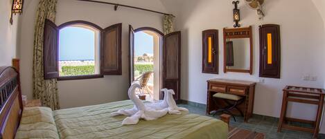 A bedroom with a bed, two open windows, a dresser, a vanity, and a fan.