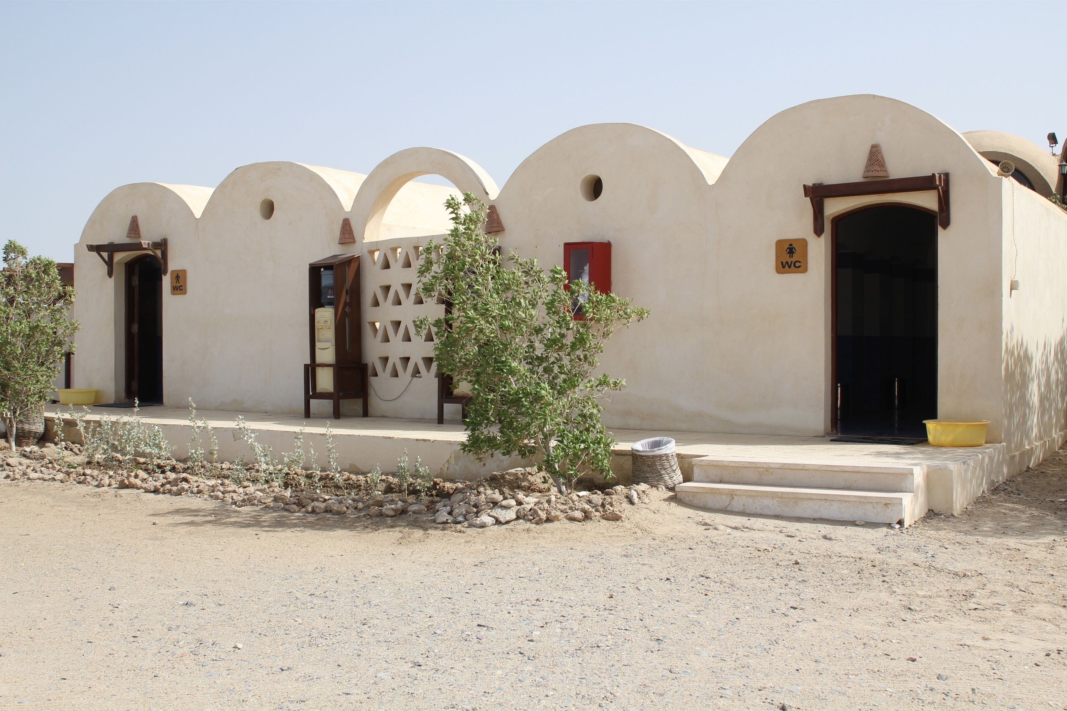 A row of buildings with arched doorways and a small tree in the foreground.