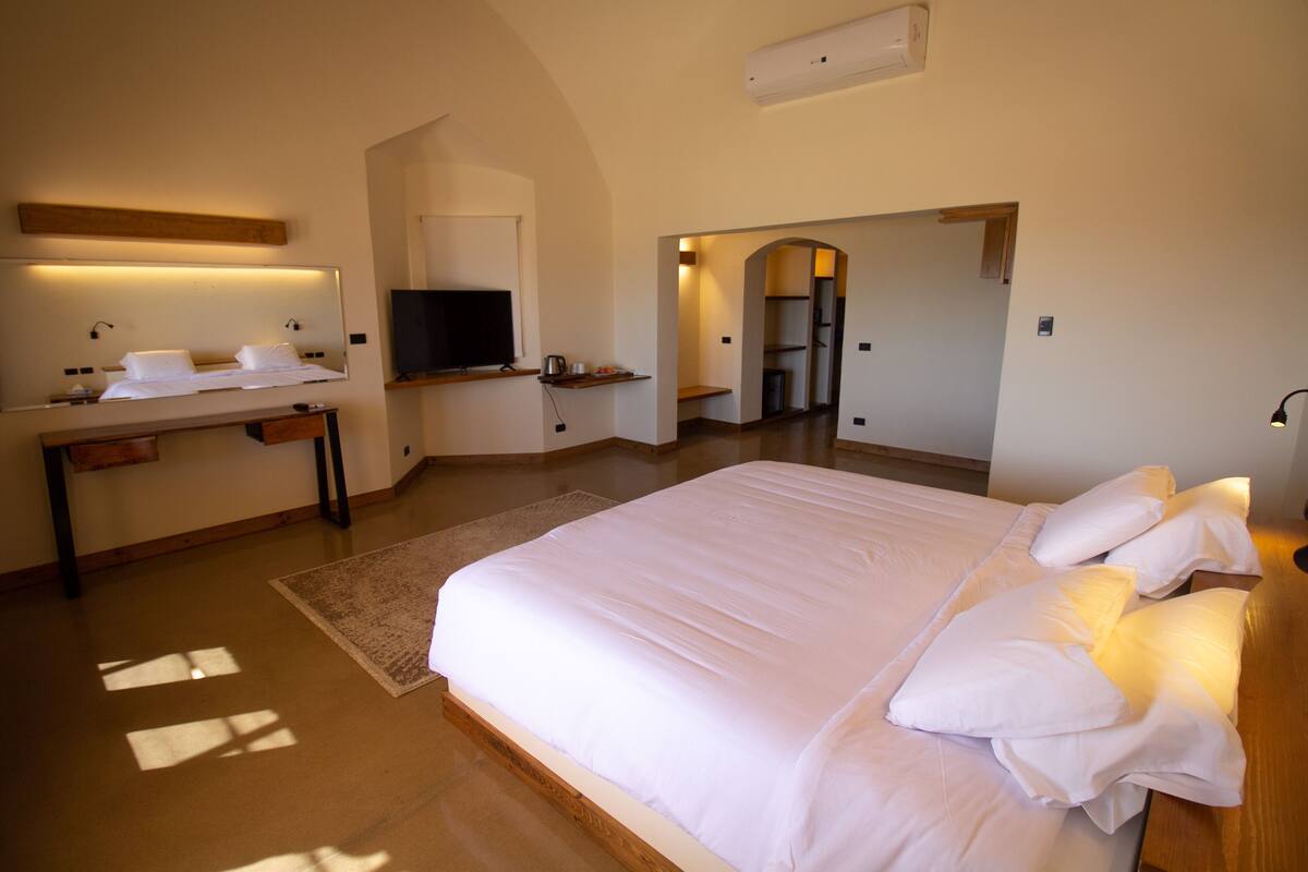 Een hotelkamer met een groot bed, een bureau met een flatscreen televisie en een spiegel boven het bed.