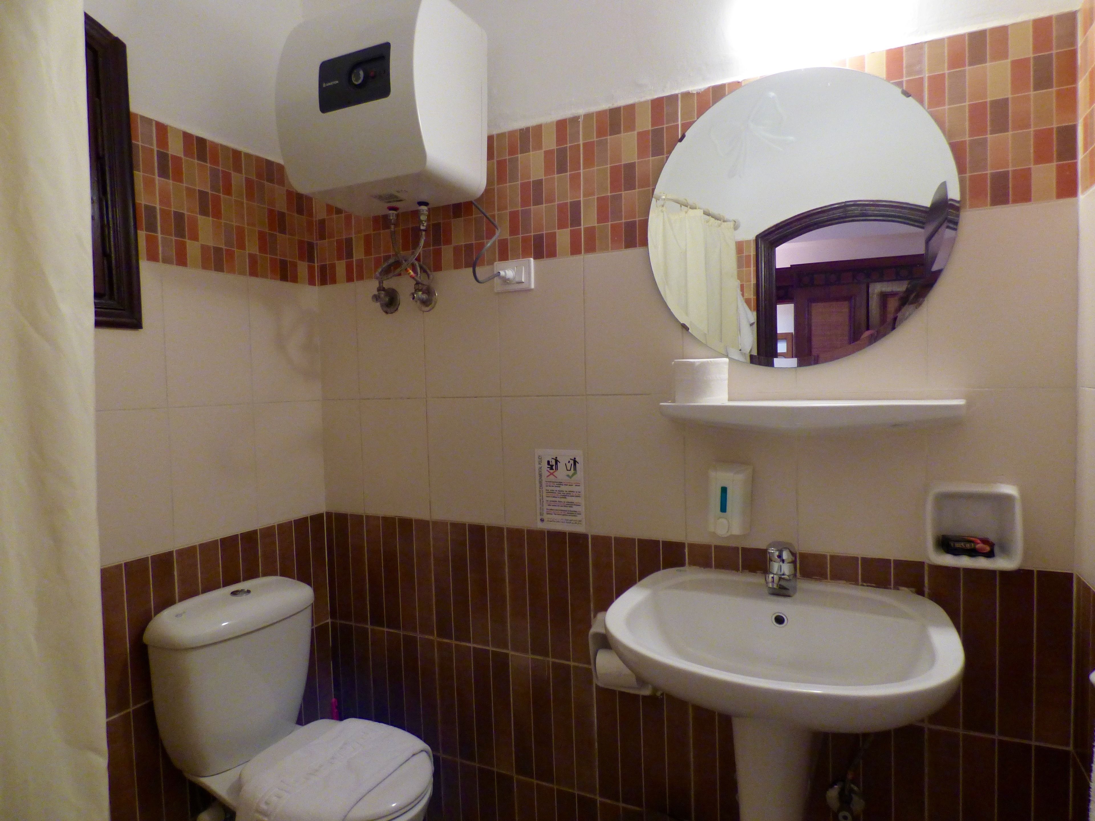 A bathroom with a toilet, sink, mirror, and towel dispenser.