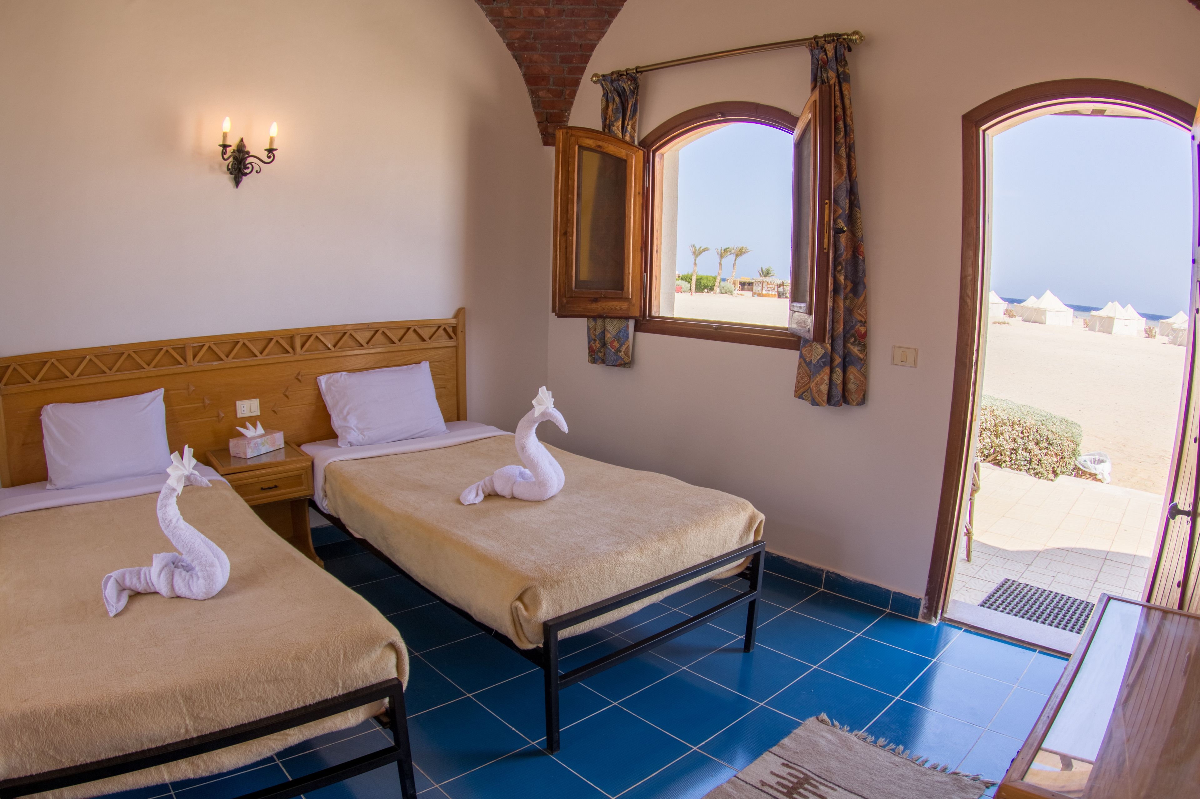 A hotel room with two beds, a window with a view of the beach, and a door leading outside.