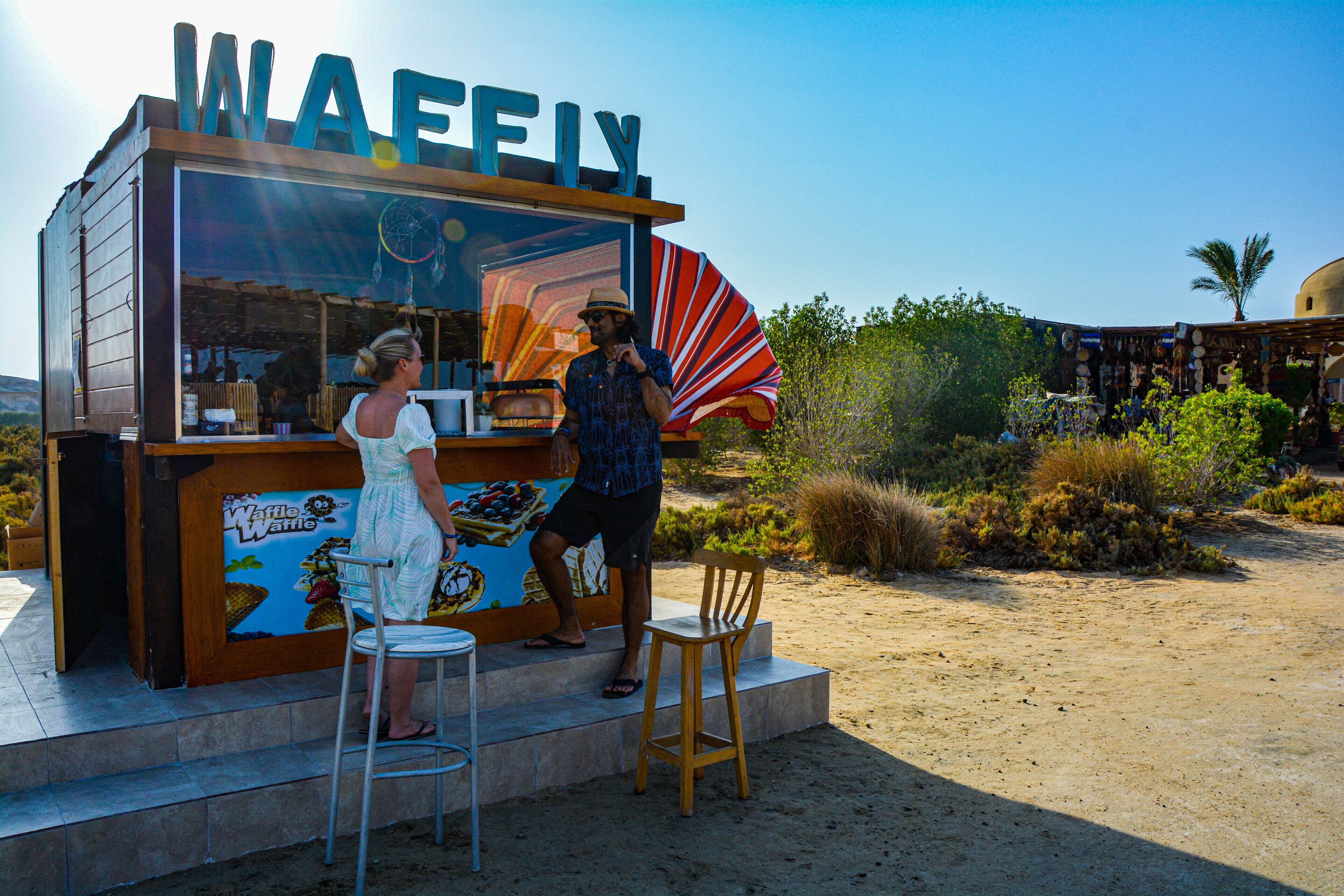 A waffle stand with a clear sign, a counter, and a seating area with a chair and a stool.