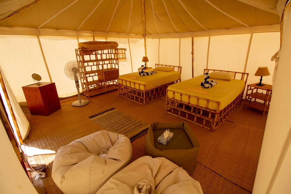 Een tentaccomodatie met twee bedden, een ventilator en een kleine tafel.