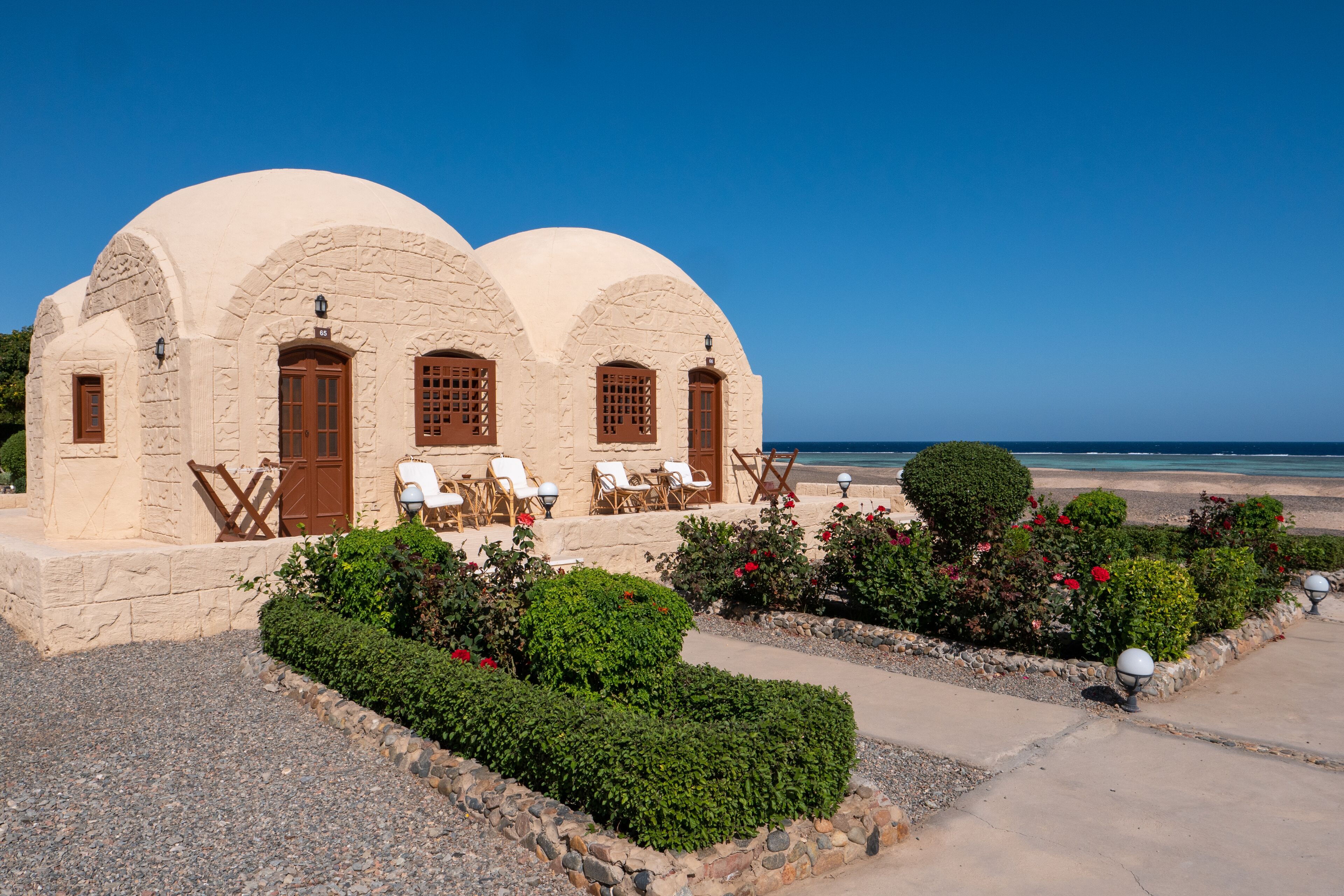 A building with three arched structures, a gravel pathway, and a beach view.
