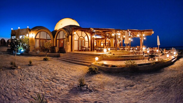A building with a dome and arched windows, outdoor seating, and a paved area. - Marsa Shagra Village (Marsa Alam)