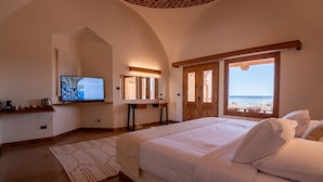 A bedroom with a large bed, a television, a mirror, and a view of the beach. - Marsa Shagra Village (Marsa Alam)