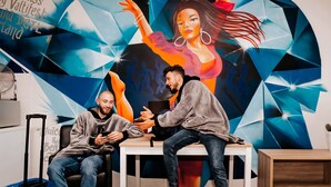 Two people sitting at a table in a room with a colorful geometric mural in the background. - Amsterdam Teleport Hotel (Amsterdam)