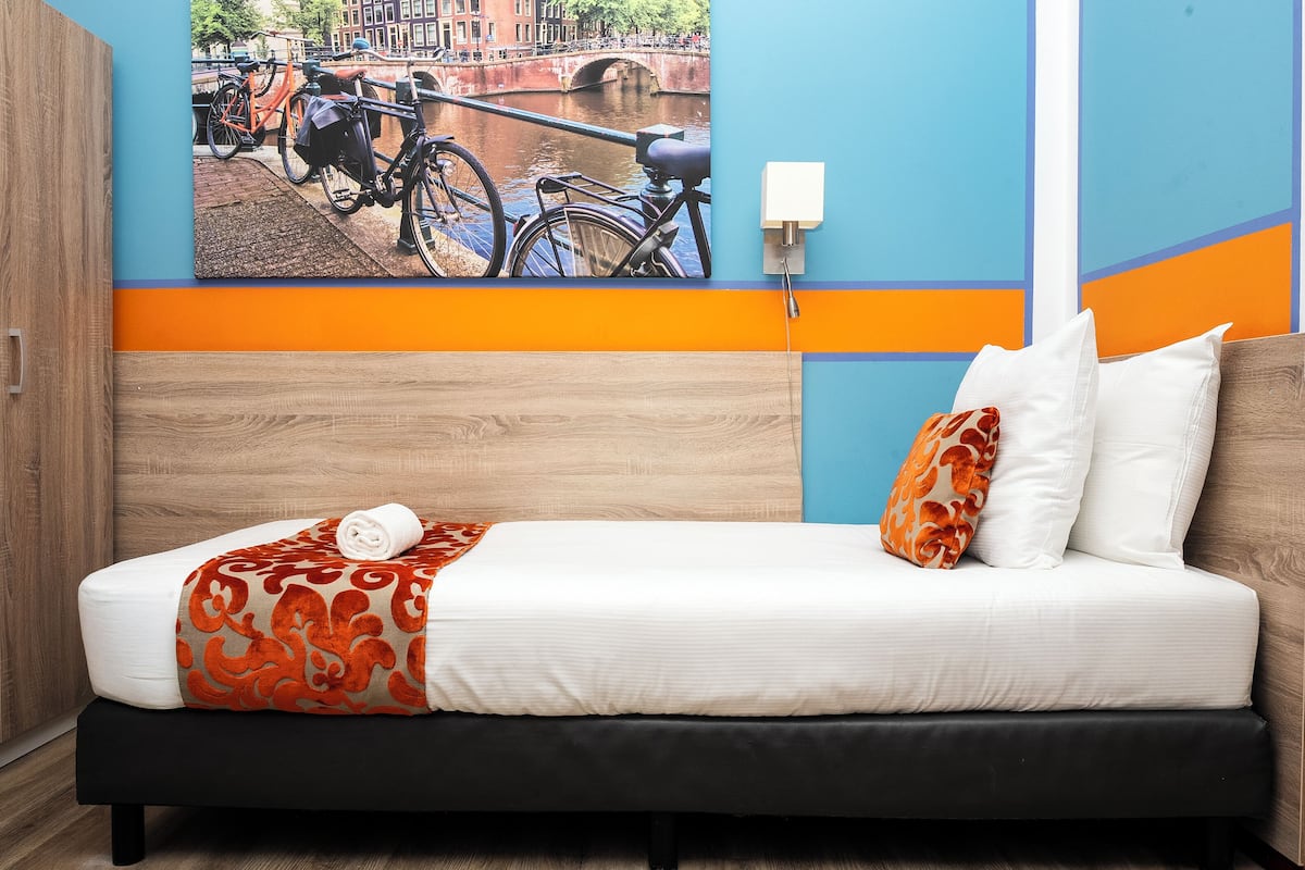 A hotel room with a bed, a view of bicycles and a bridge, and a wall-mounted lamp.