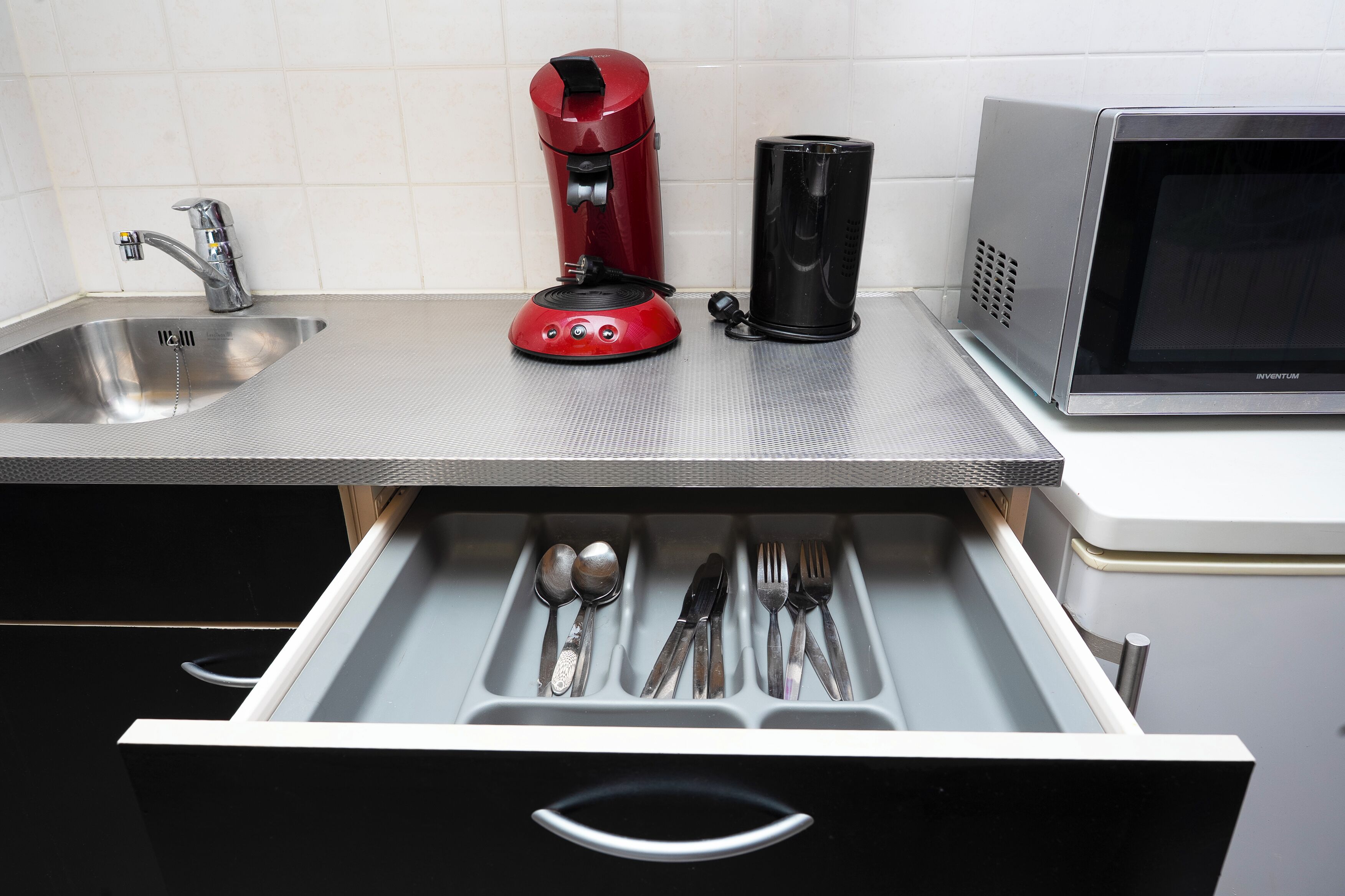 A kitchen with a stainless steel sink, a red coffee maker, a black coffee pot, and a microwave.