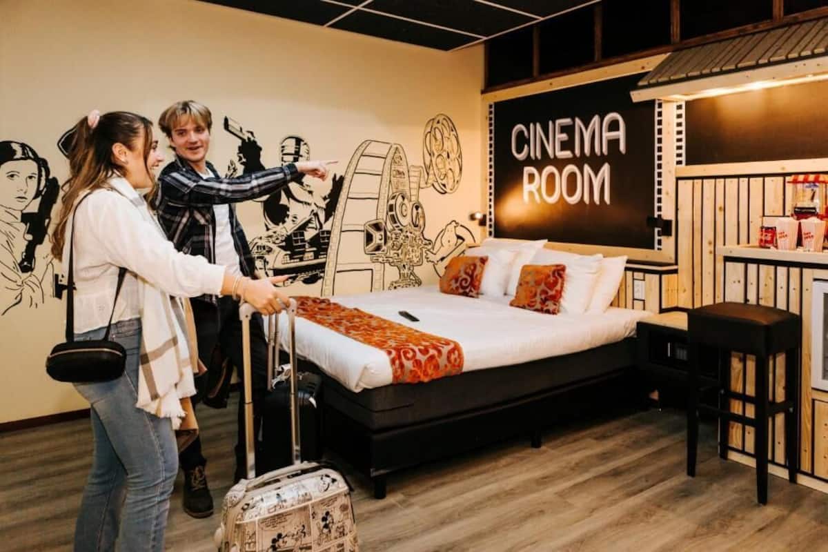 A bedroom with a bed, a suitcase, and a wall with a cinema room sign.