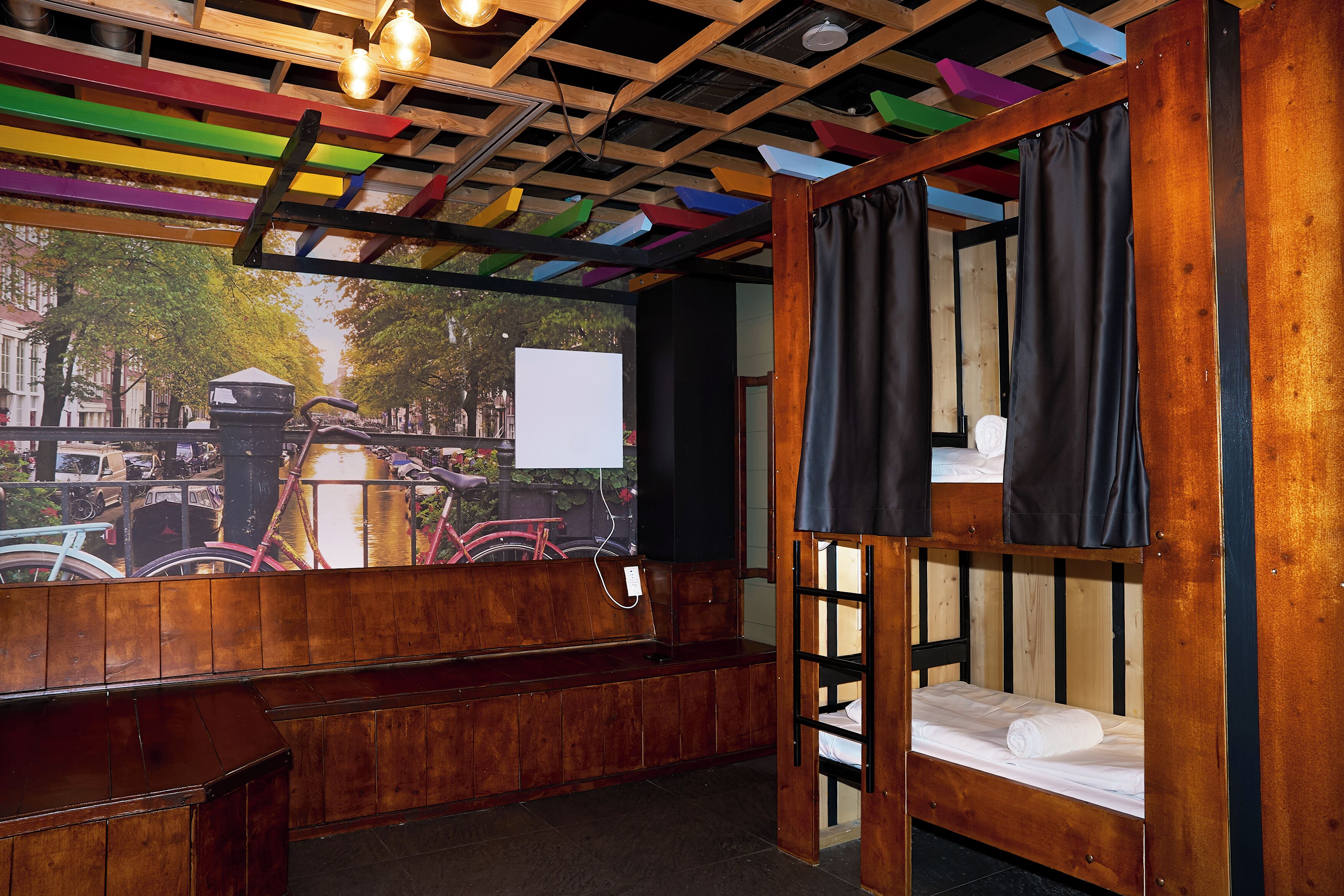 A room with a wooden bunk bed, a bench, and a view of bicycles and trees through a large window.