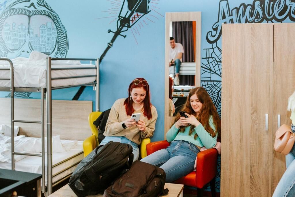 Een studentenkamer met stapelbedden, een spiegel en een muur met een stadsgezichtsmural.