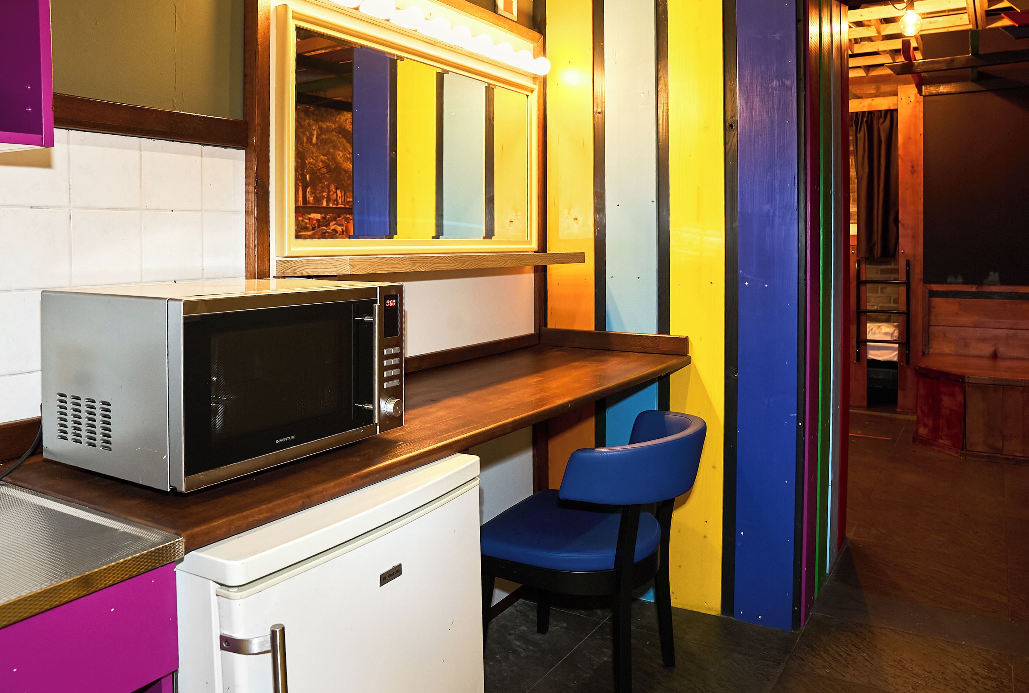 Une cuisine compacte équipée d’un four à micro-ondes, d’un petit réfrigérateur et d’une chaise bleue.