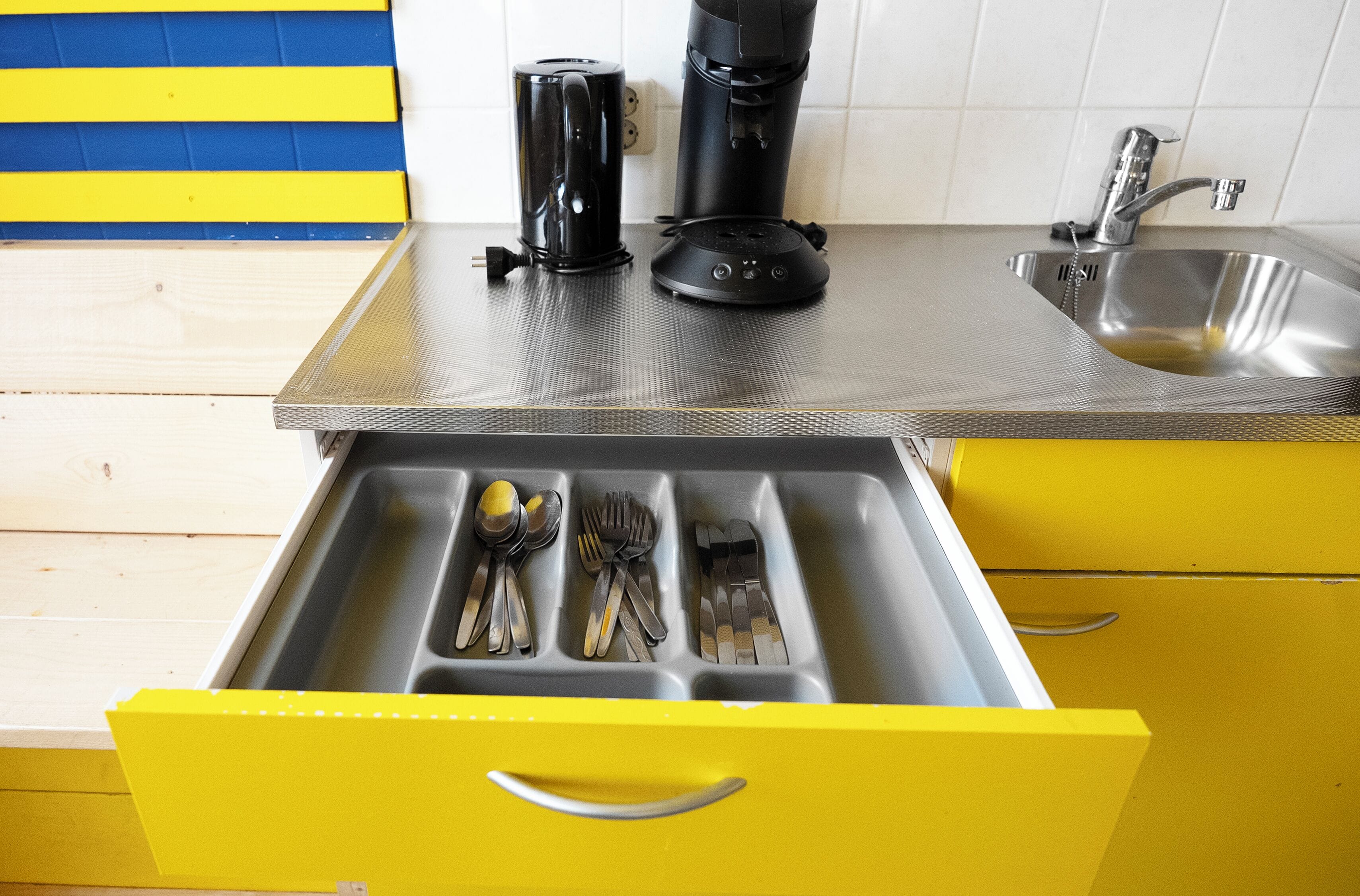 Een keuken met een roestvrijstalen spoelbak, een koffiezetapparaat en bestek in een lade.