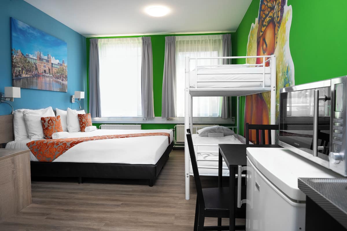 A hotel room with a bunk bed, a desk, and a chair. There is a painting on the wall and a window with curtains.